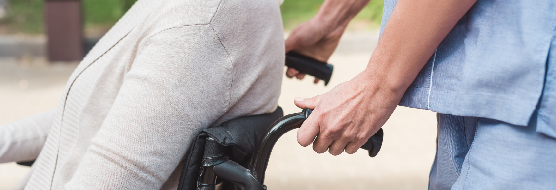 Pflegende schiebt eine Person im Rollstuhl.